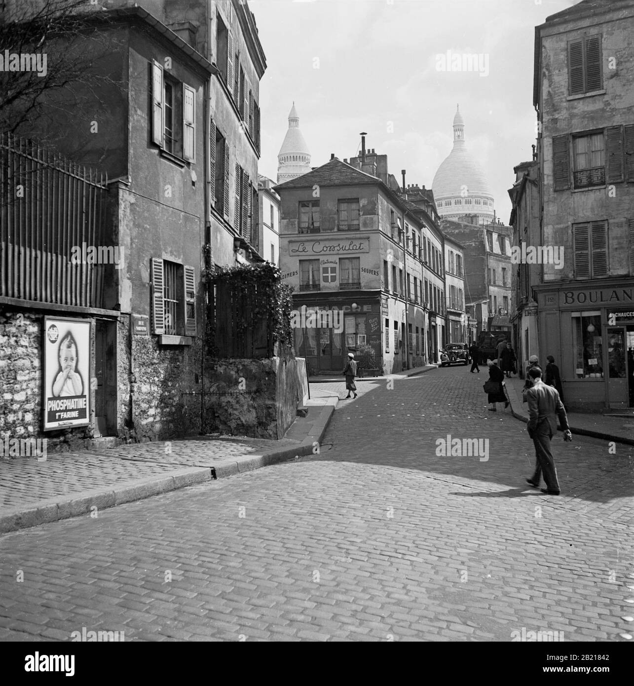 Années 1950, Paris, France, rue pavée dans le quartier de Montmartre de la ville parisienne, célèbre pour ses artistes de rue et son église, Sacré-cœur. L'image montre les rue des ventes et le restaurant, le Consulat avec les dômes du Sacré-cœur en arrière-plan. Banque D'Images