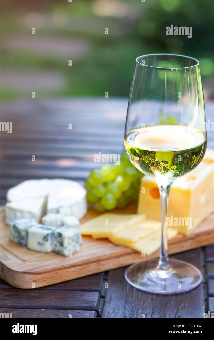 Élégant verre de vin blanc sur table en bois avec des tranches de fromages et de raisin différents avec des plantes vertes sur fond flou Banque D'Images