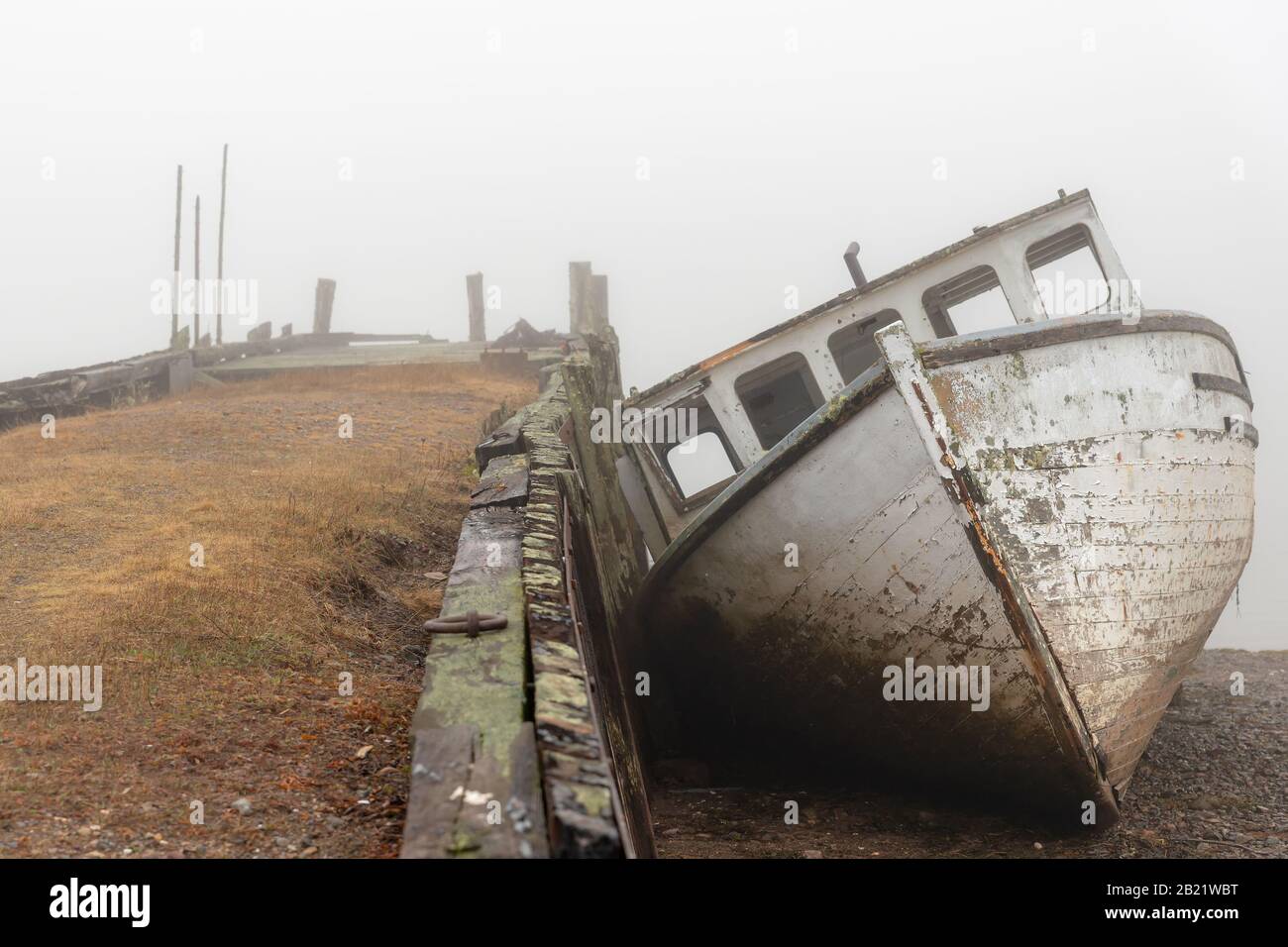 Un bateau naufragé sur la rive à côté d'un vieux quai abandonné en une journée très molle. Le bateau est en très mauvais état et tombe en dehors. Marée basse. Banque D'Images