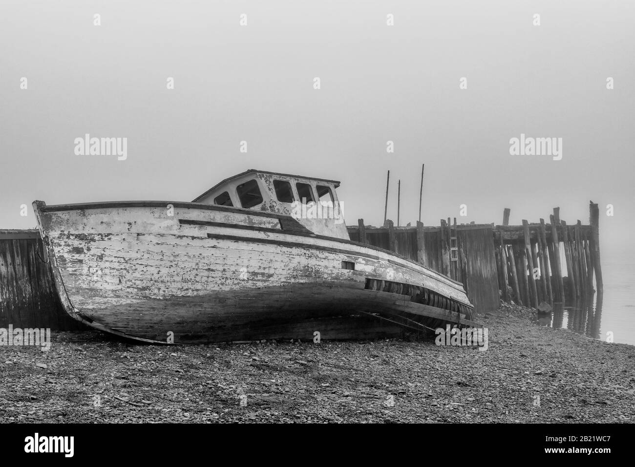 Un bateau naufragé sur la rive à côté d'un vieux quai abandonné en une journée très molle. Le bateau est en très mauvais état et tombe en dehors. Marée basse. Banque D'Images