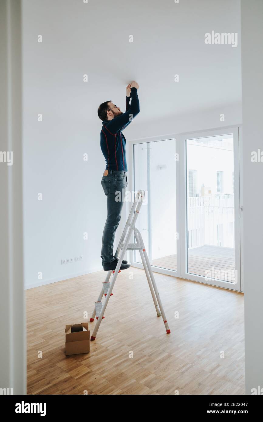 propriétaire de maison debout sur l'échelle de fixation de l'éclairage installation Banque D'Images