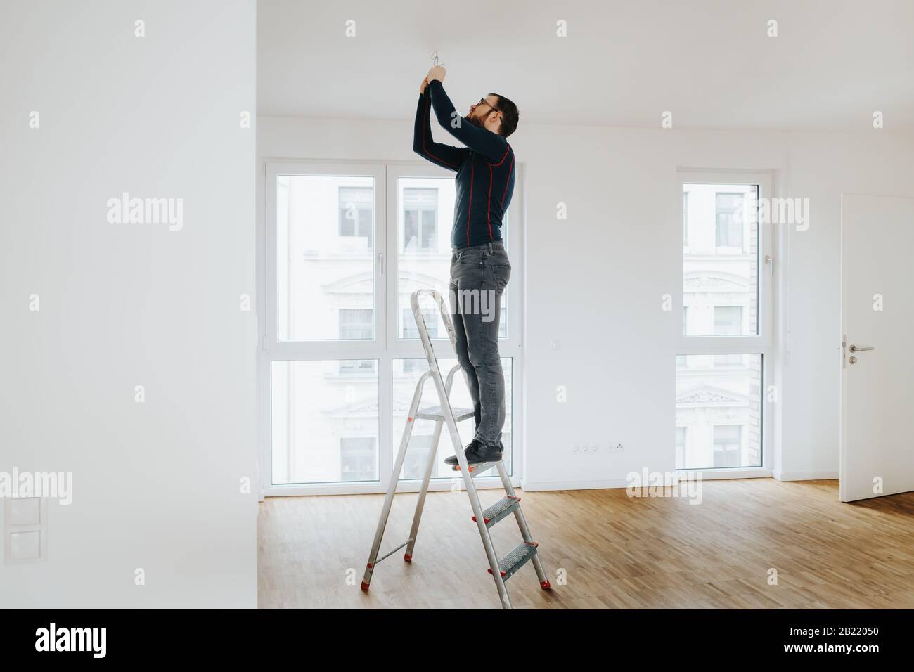 propriétaire de maison debout sur l'échelle de fixation de l'éclairage installation Banque D'Images