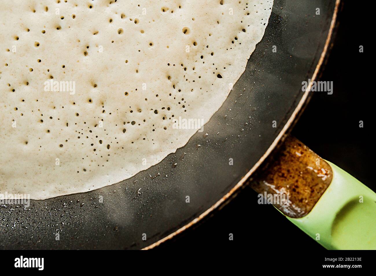 Une crêpe à base de pâte liquide avec bulles est frite dans une poêle noire  avec des gouttes de graisse et d'huile sur une cuisinière à induction Photo  Stock - Alamy