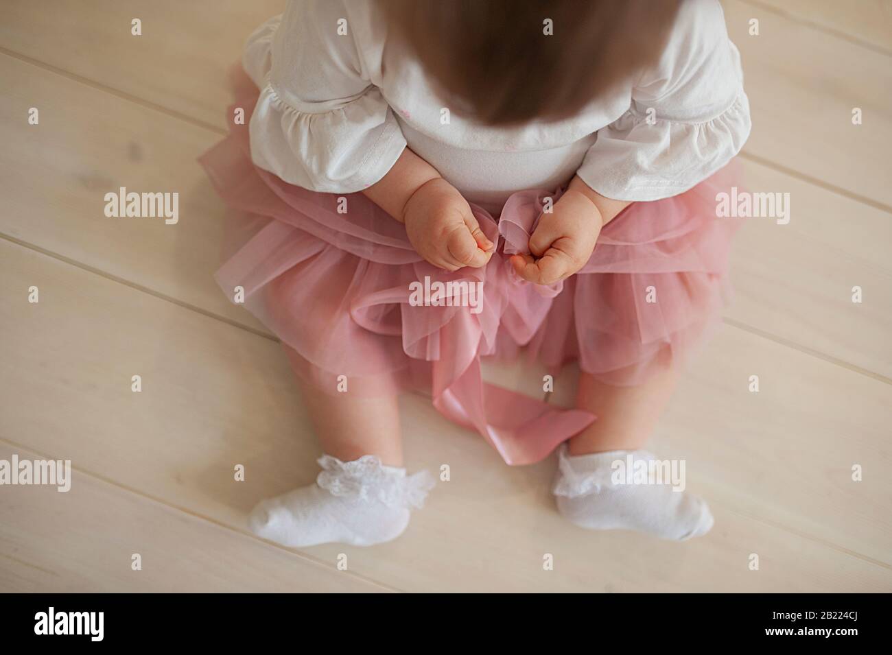 une fillette dans une jupe en tulipe rose poussiéreuse, des chaussettes en dentelle blanche, aux bras gonflés, se trouve sur un sol en bois de couleur claire Banque D'Images