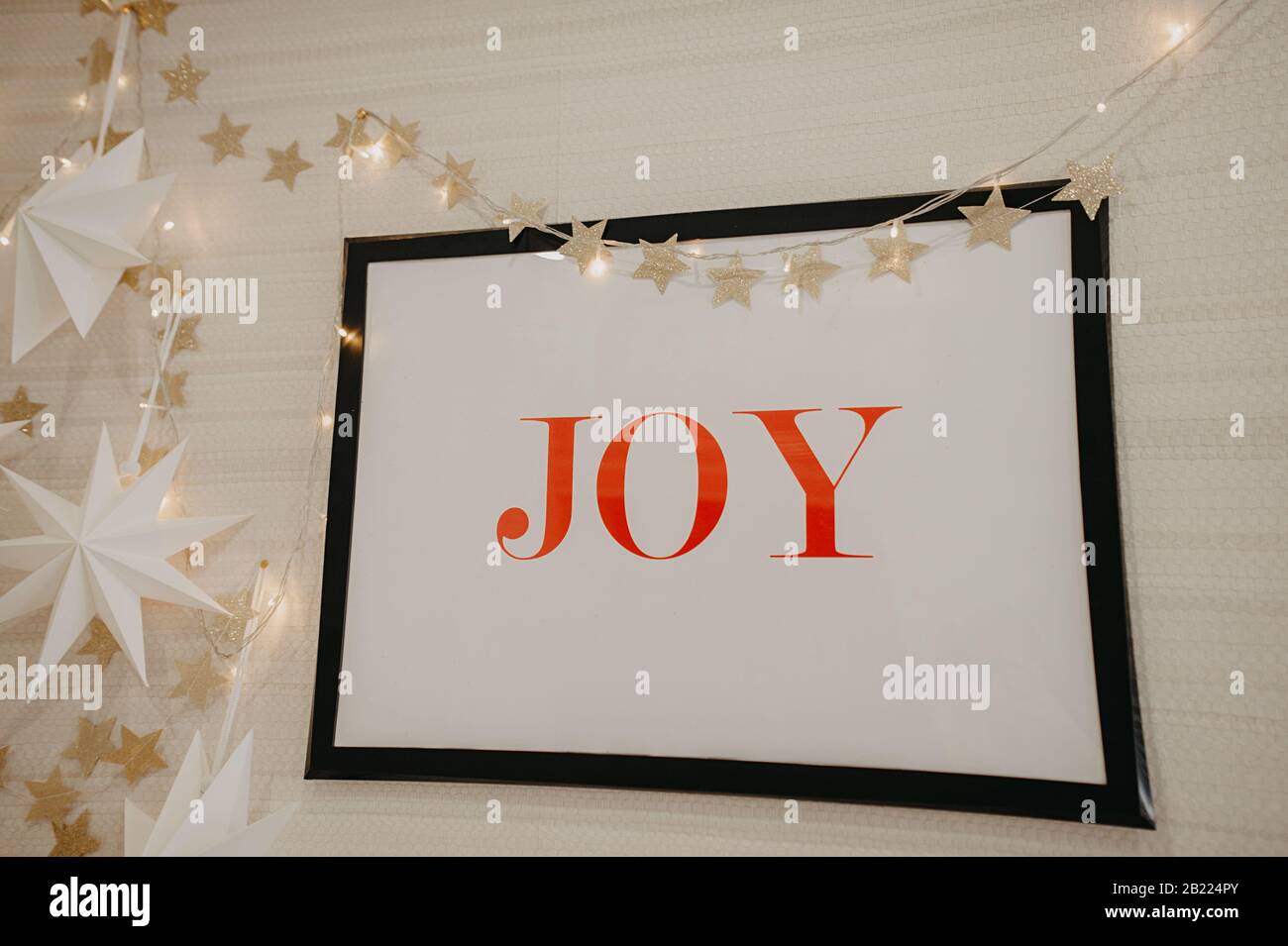 Décoration murale pour Noël, une grande photo avec UNE JOIE d'inscription rouge, sur un fond de guirlandes et d'étoiles de couleur or Banque D'Images