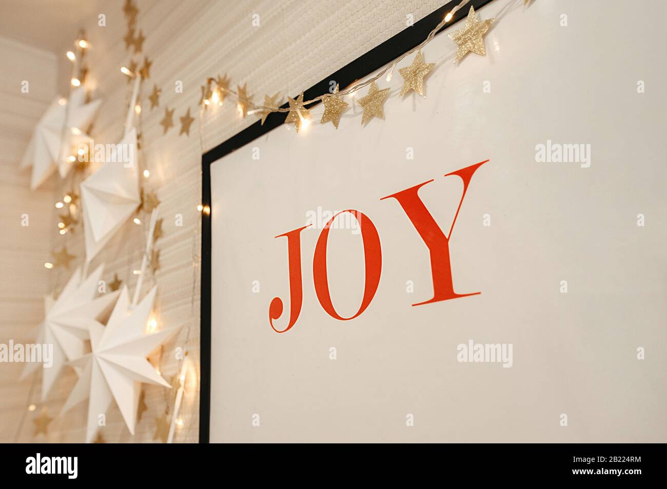 Décoration murale pour Noël, une grande photo avec UNE JOIE d'inscription rouge, sur un fond de guirlandes et d'étoiles de couleur or Banque D'Images