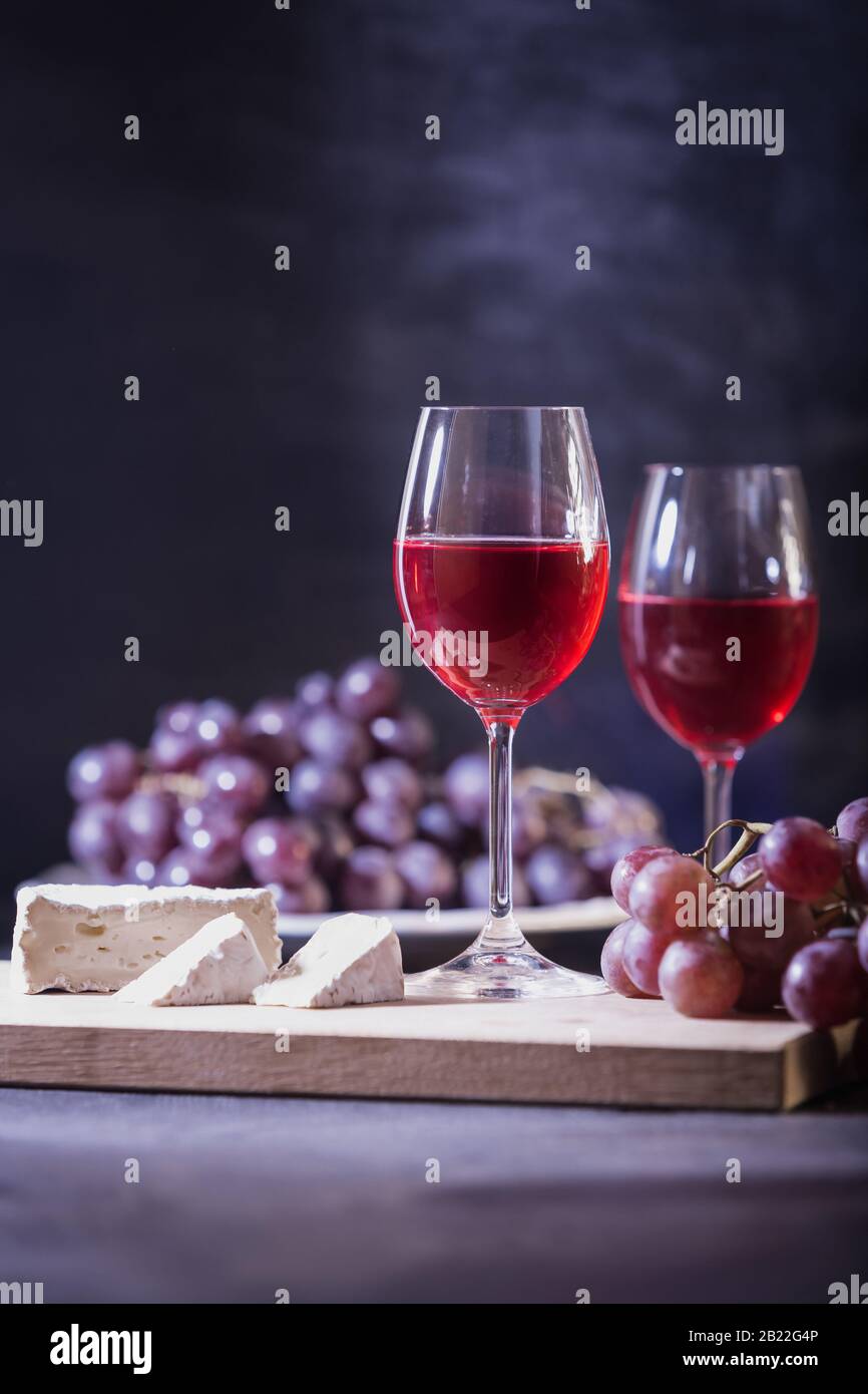 Un verre de vin de fruits rouges. Gros plan de la vigne et du fromage de brie sur un fond bleu foncé en touche basse. Espace de copie. Bannière pour café, domaine viticole. Banque D'Images
