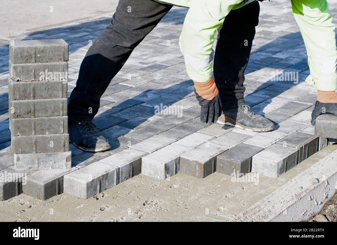 Le maître en gants pose des pavés en couches. Pavage de la voie de la brique de jardin par un ouvrier de finisseur professionnel. Pose de dalles de béton gris sur du sable Banque D'Images