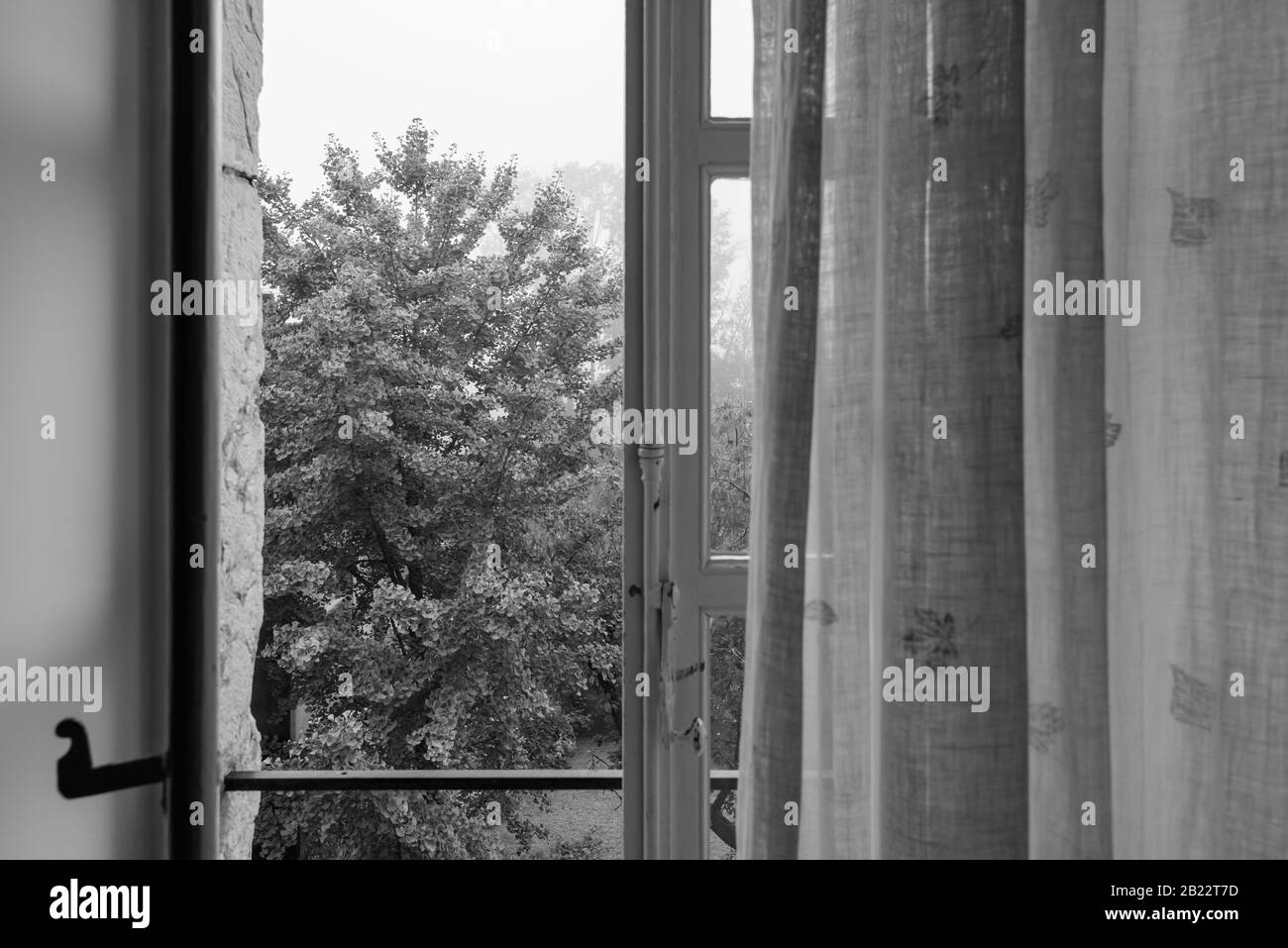 Vue sur le jardin à travers une fenêtre en bois traditionnelle ouverte dans un petit château de l'est de la France, le matin de septembre. Banque D'Images