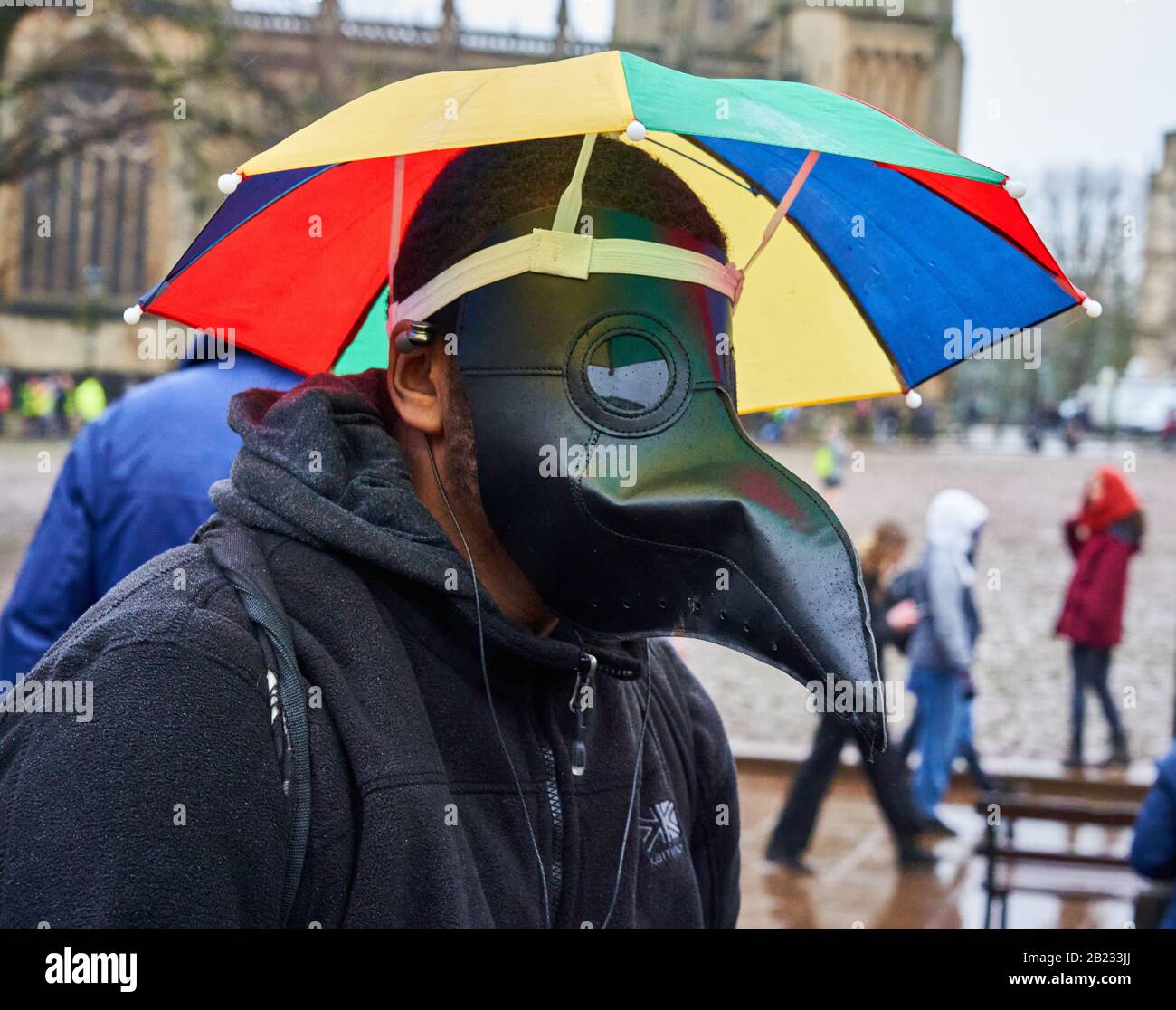 Homme dans le masque de médecin anti-peste de Coronavirus avec parapluie attaché à Greta Thunberg Mars pour Climat et SchoolStrike Bristol Royaume-Uni Février 2020 Banque D'Images