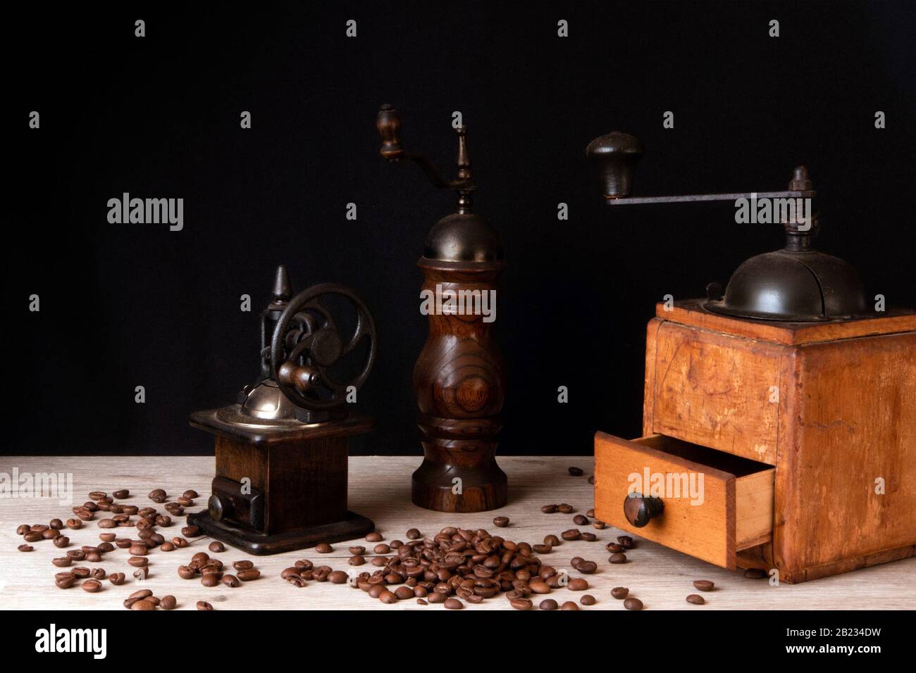 Moulins à café et moulin à poivre anciens en bois avec des grains de café dispersés sur une surface en bois Banque D'Images