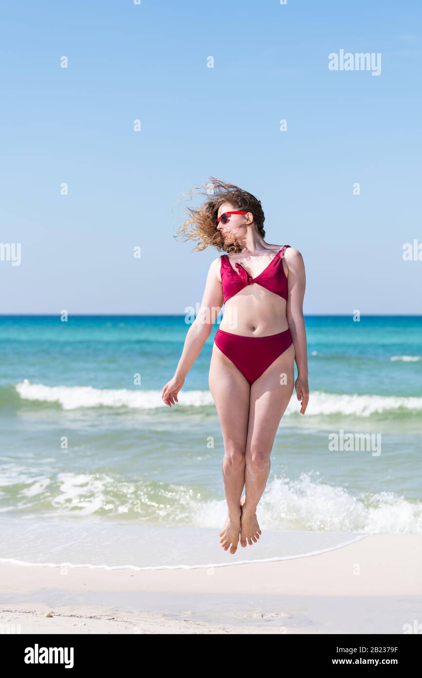 Jeune fille femme en maillot de bain rouge lunettes de soleil sautant avec  l'eau de mer verte en arrière-plan à Santa Rosa Beach et horizon Photo  Stock - Alamy