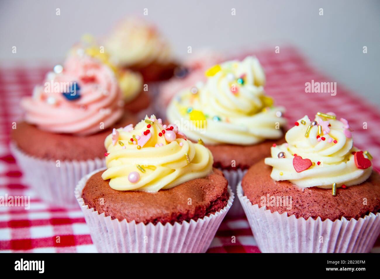 Gâteaux de tasse en velours rouge avec garniture blanche et rose à partir d'une crème de beurre frais. Avec de petites têtes colorées comme une ancre ou aussi de l'ananas. Banque D'Images