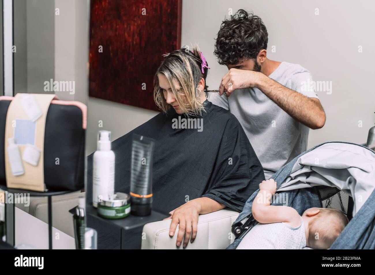 Maitre Coiffeur Coupe Les Cheveux De Femme Blonde Bebe Dans Le Bebe Alors Que La Mere A La Coupe De Cheveux Dans Le Salon Photo Stock Alamy