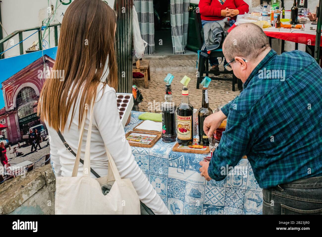 Vendeur de rue de sexe masculin servant de la liqueur de cerise aigre Ginjinha en plein air à une femme à alfama lisbonne portugal Banque D'Images