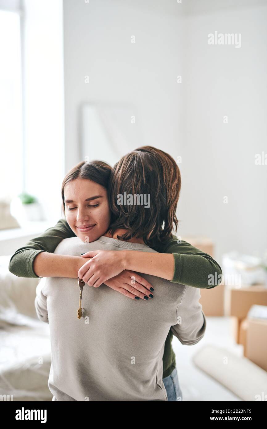 Une jeune femme heureuse avec la clé d'un nouvel appartement donnant Hug à son mari tout en se tenant dans l'une des chambres de leur nouvel appartement ou maison Banque D'Images