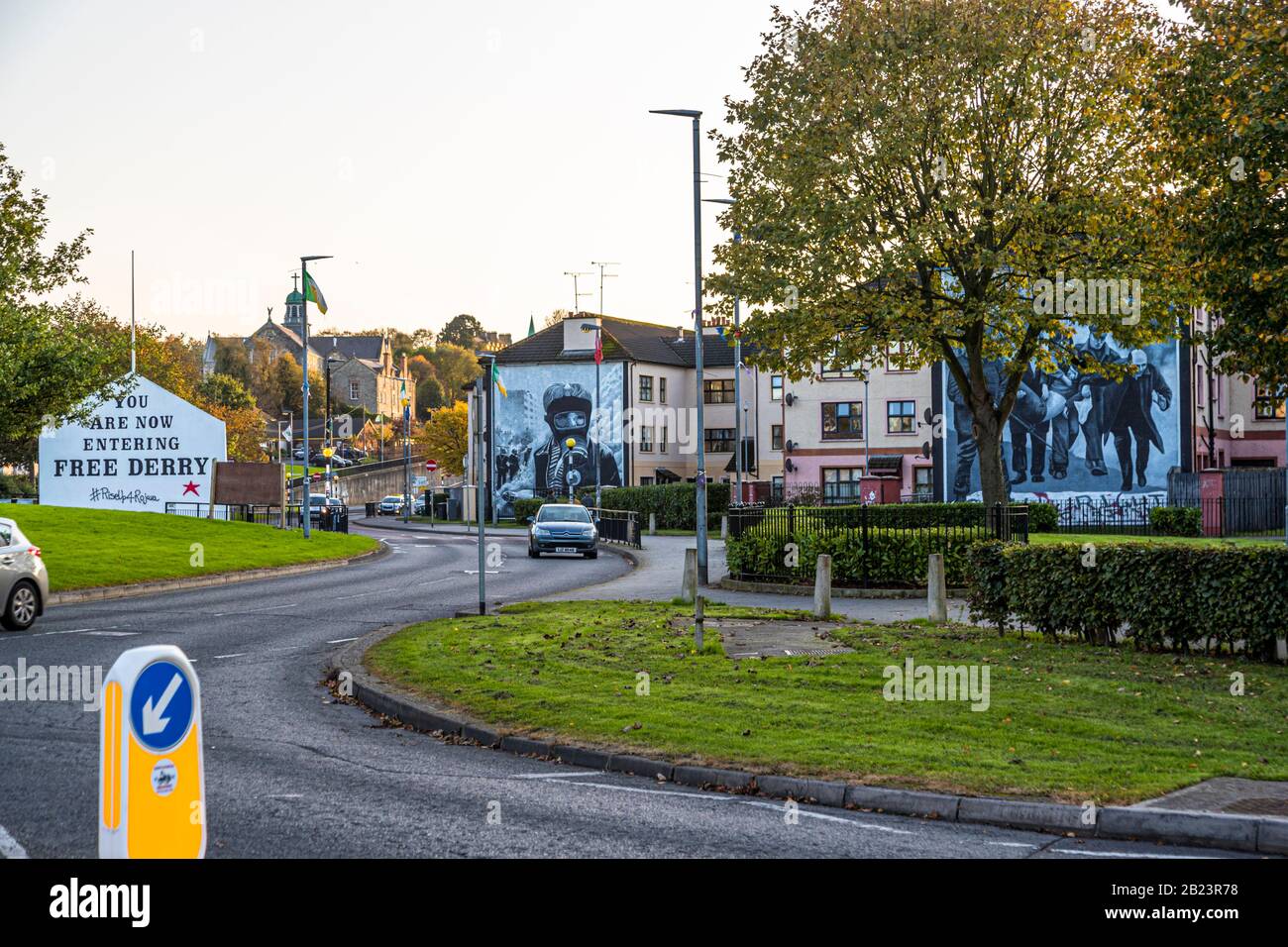 Free Derry Corner (à gauche) et la fresque du Petrol Bomber (à droite) encadrent Rossville Street dans le quartier de Bogside à Londonderry, comté de Derry, Irlande du Nord ; une tour d'église est visible en arrière-plan. Banque D'Images
