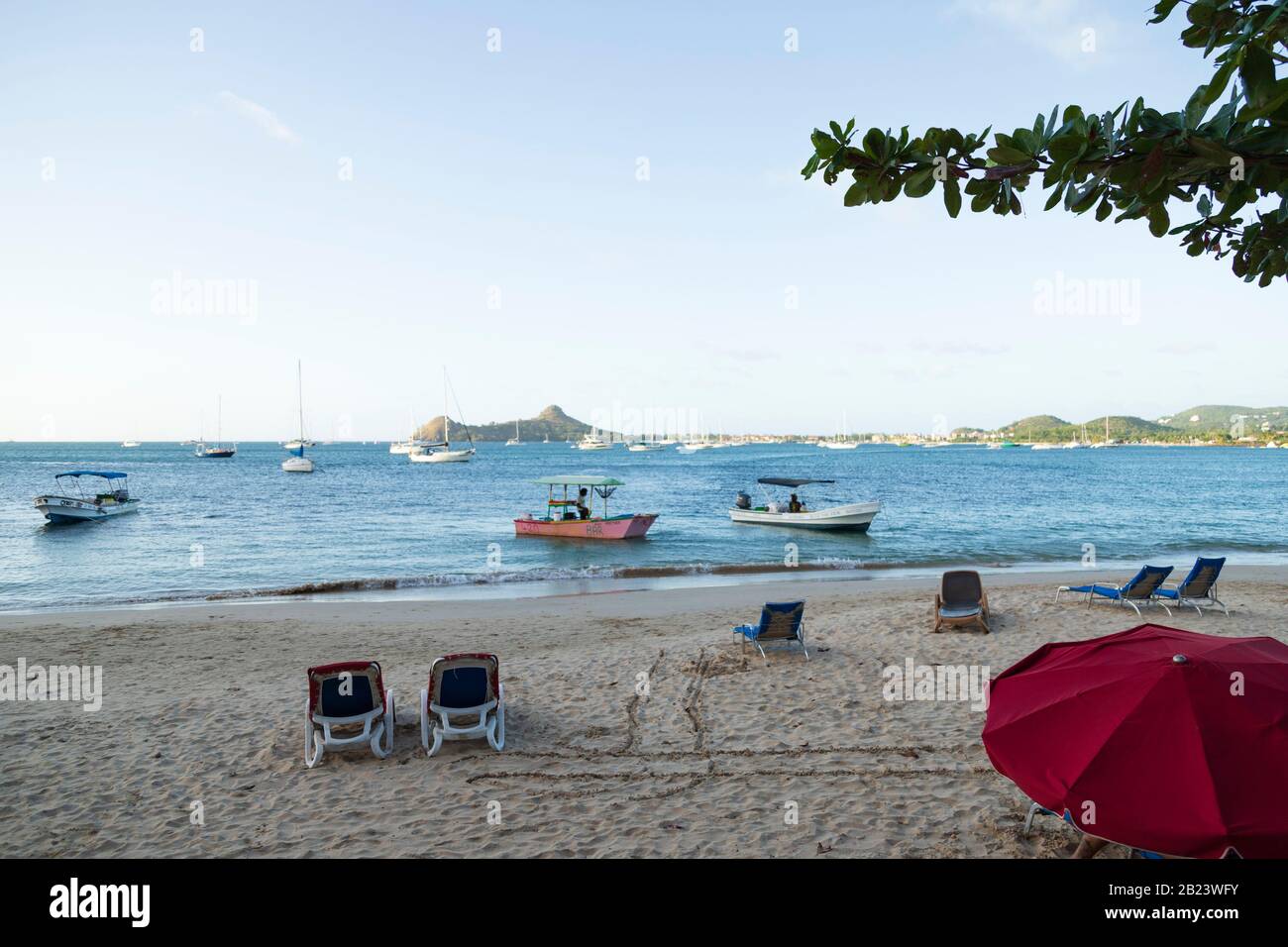 Embellissez la journée lumineuse à la plage, des chaises de plage vides, un parasol et des bateaux de pêche près de la rive à Reduit Beach, gros Islet, Sainte-Lucie Banque D'Images