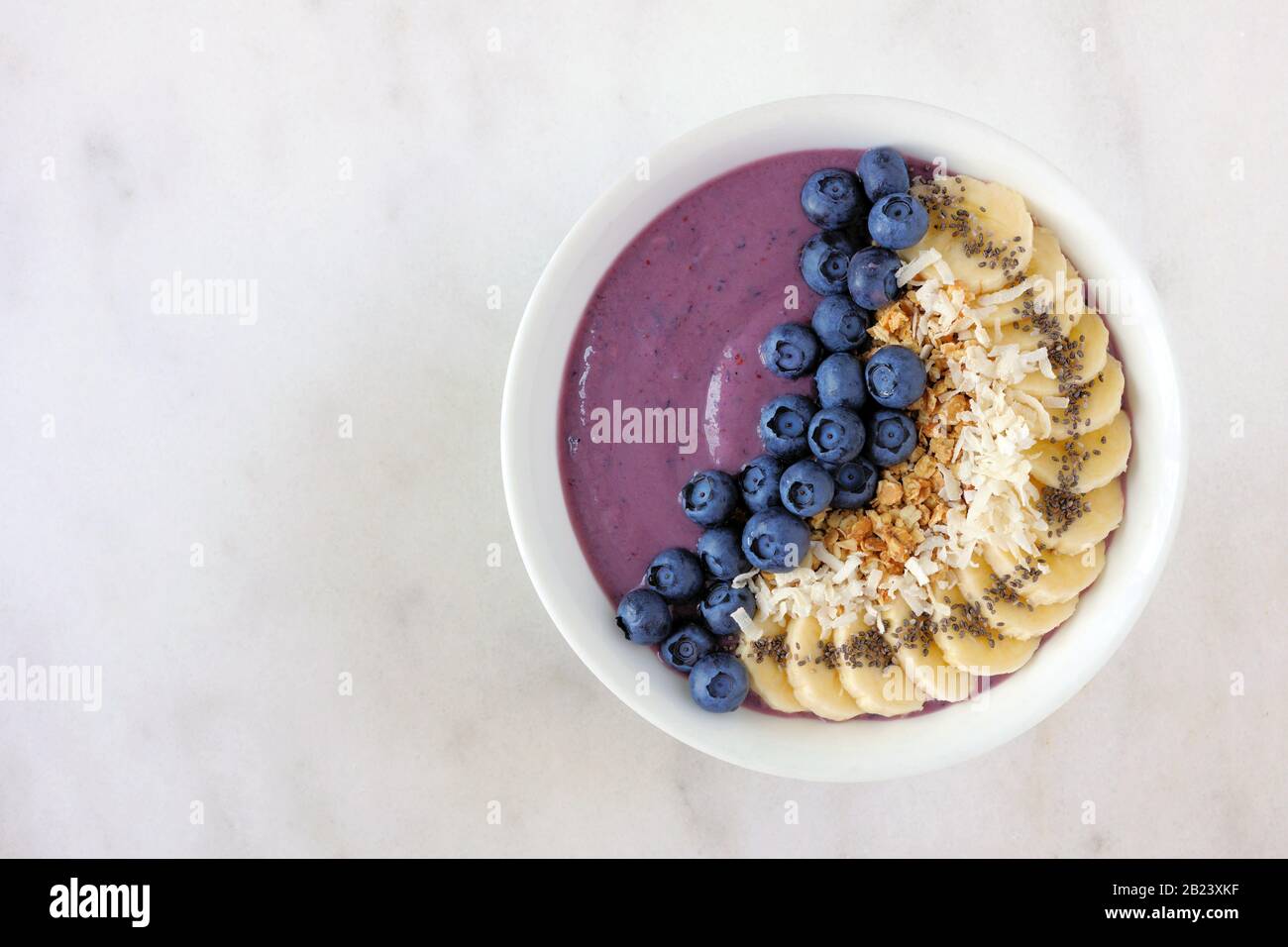 Bol à smoothie sain aux bleuets avec noix de coco, bananes, graines de chia et granola. Vue de dessus sur un arrière-plan lumineux. Banque D'Images