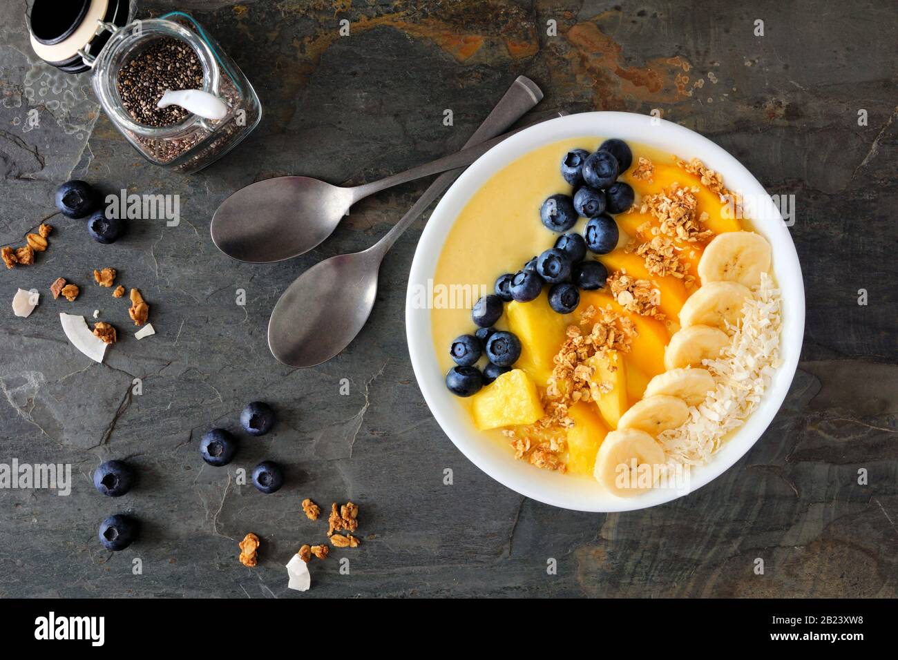 Bol d'ananas sain, de smoothie à la mangue avec noix de coco, bananes, bleuets et granola. Vue au-dessus sur un fond sombre. Banque D'Images