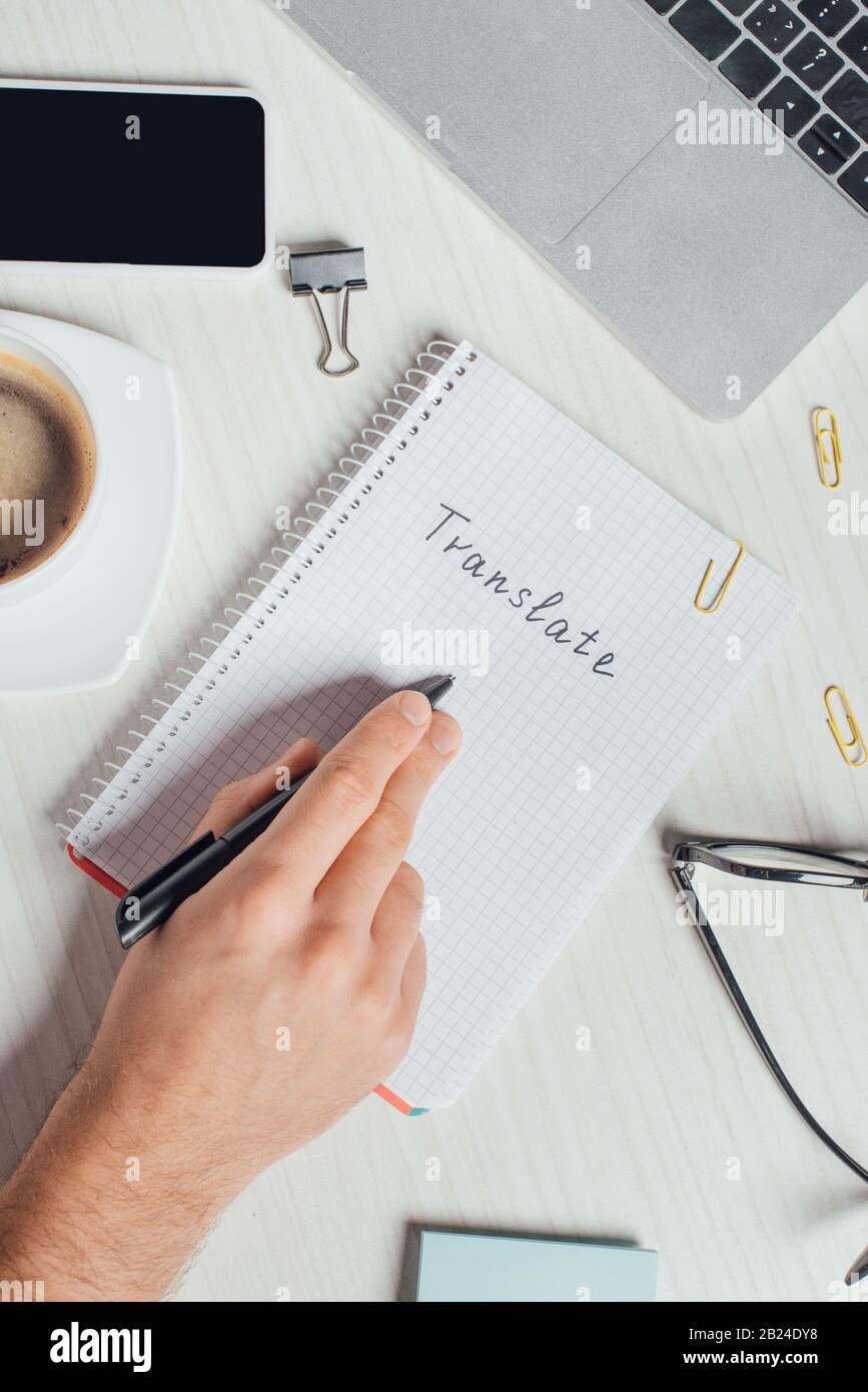 vue partielle du traducteur travaillant avec le bloc-notes, l'ordinateur portable et le smartphone sur le lieu de travail avec une tasse de café Banque D'Images