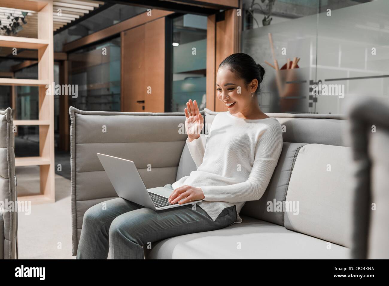 une femme d'affaires asiatique heureuse qui se réveinait tout en restant assise sur le canapé et en discutant vidéo sur un ordinateur portable Banque D'Images