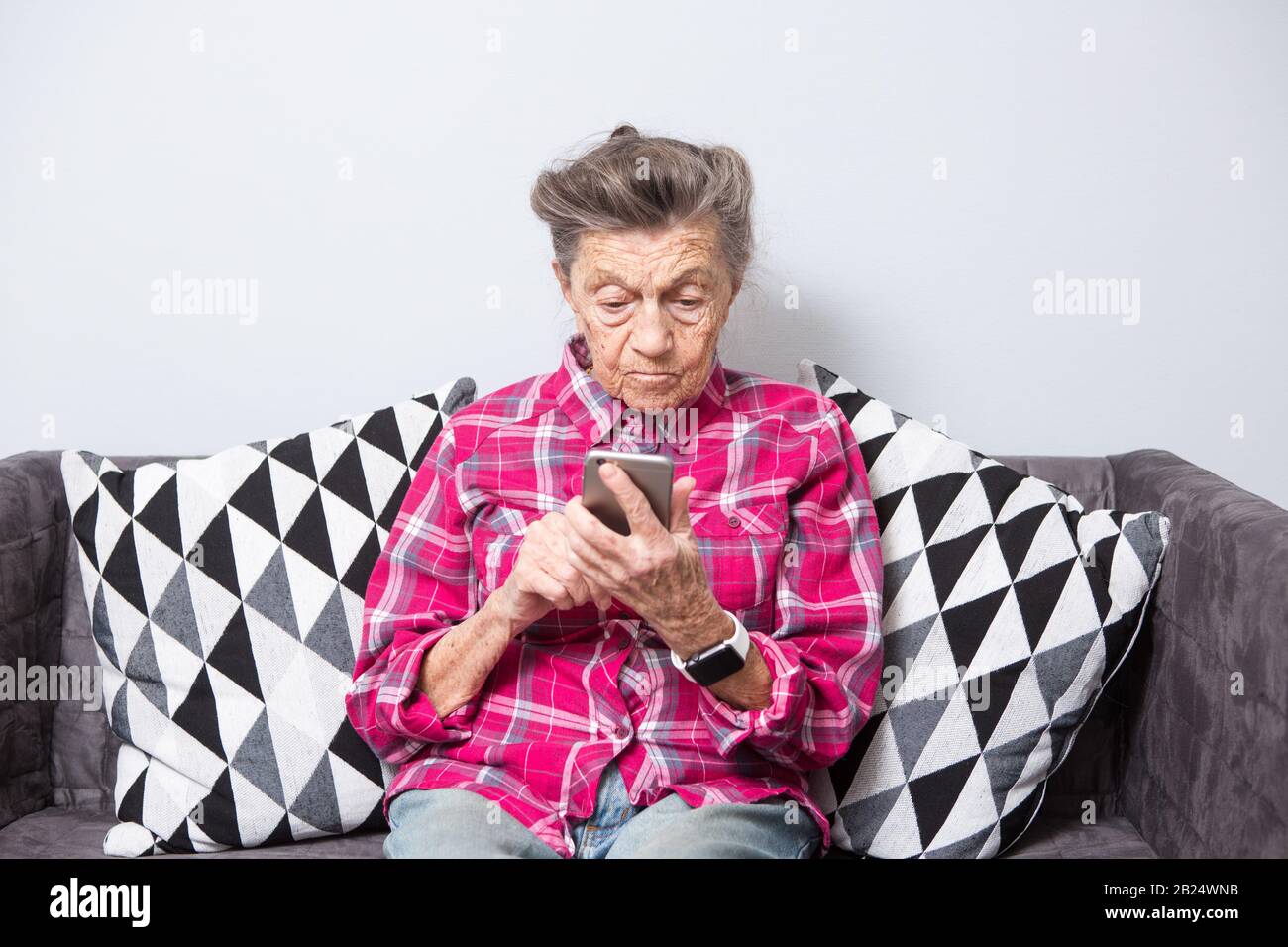 Vieux thème personne utilise la technologie. vieille femme aux cheveux gris et blancs avec les rides se trouve accueil dans la salle de séjour sur le canapé et utilise votre téléphone mobile en mains, l'air Banque D'Images