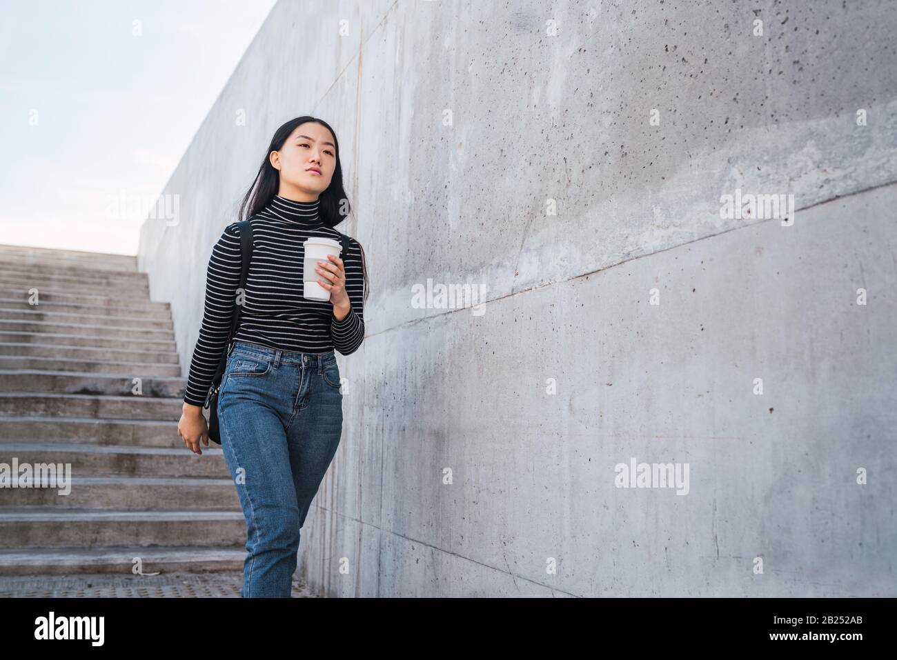 Portrait of young Asian woman holding une tasse de café à emporter contre en béton. Banque D'Images