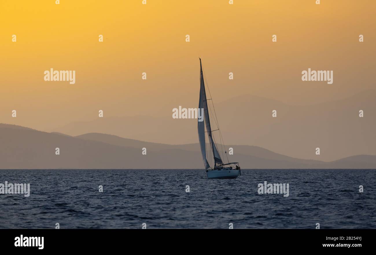 Bateau à voile en mer ouverte à l'heure d'or en soirée. Montagnes Silhouette en arrière-plan. Aventure estivale, vacances actives en Méditerranée Banque D'Images
