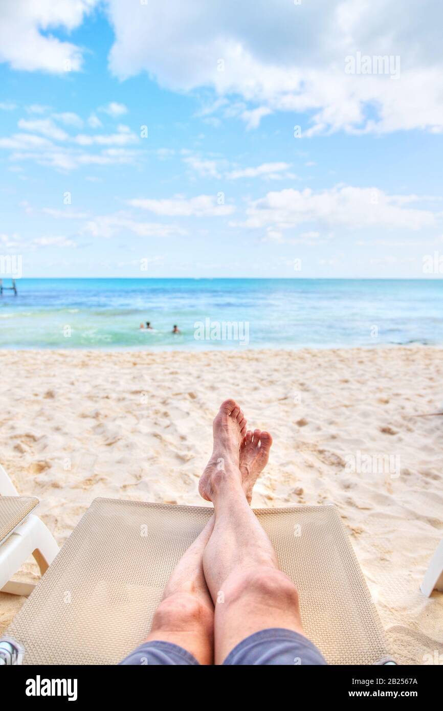 Point de vue personnel de l'homme se reposant sur une chaise longue sur une plage de sable avec vue sur les jambes croisées vers la vue sur la mer et espace de copie. Tir pris dans les Caraïbes Banque D'Images