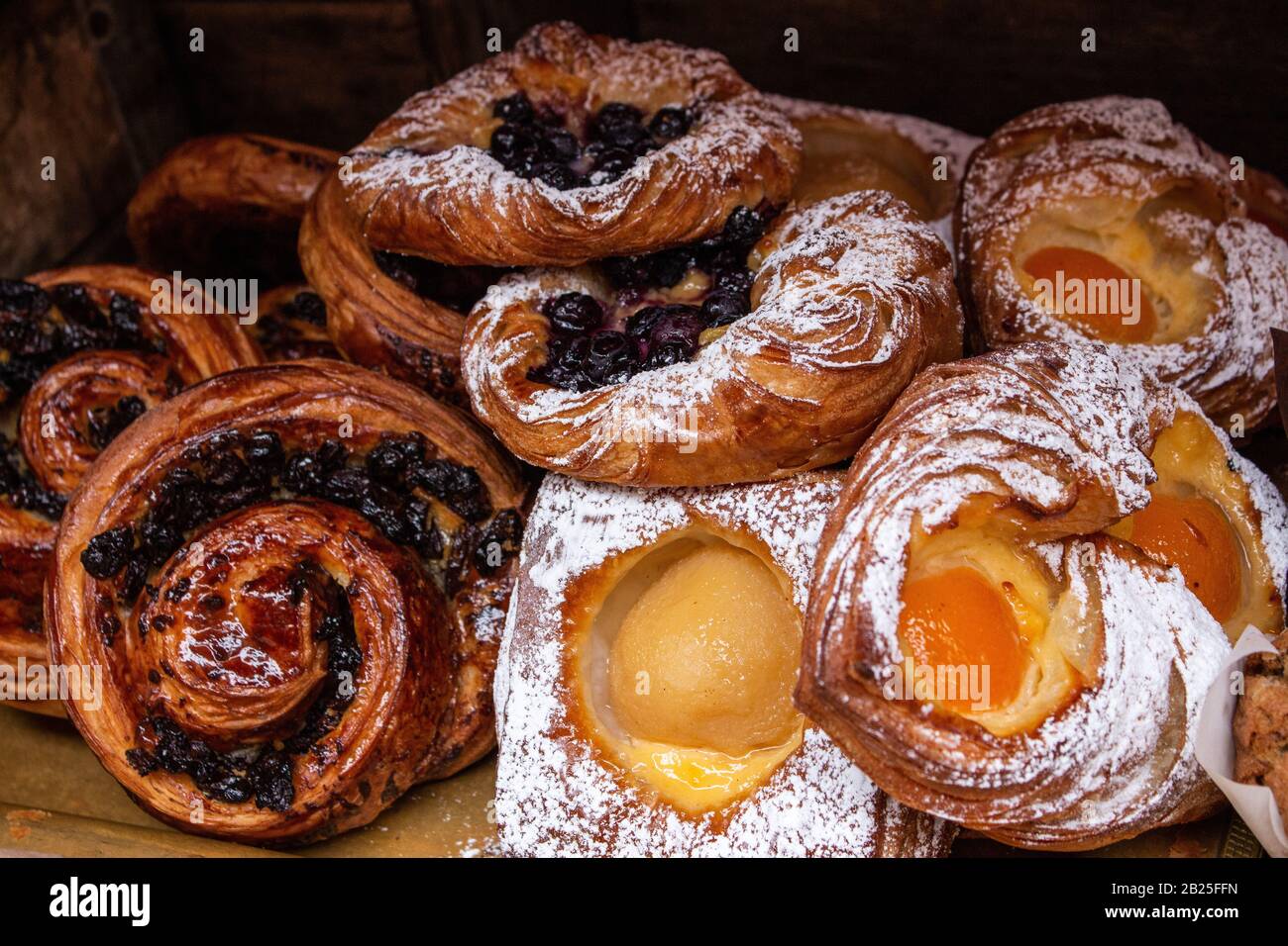 Pâtisseries danoises fraîchement cuites, crème anglaise, abricots, bleuets, raisins secs, spirales de cannelle cuites dans du sucre glace et du glacer Banque D'Images