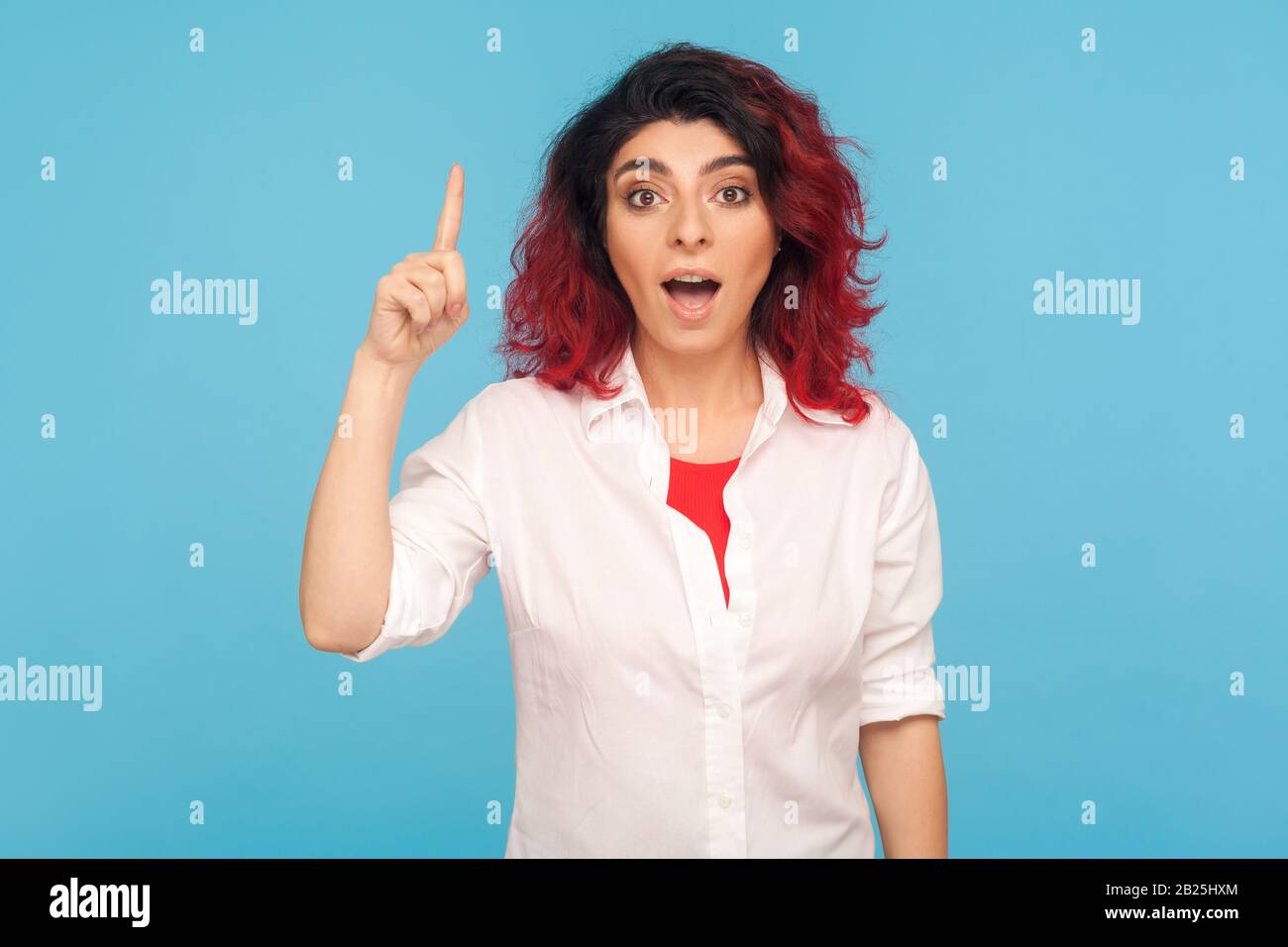 Pensée intelligente. Portrait de fille hipster avec des cheveux rouges fantaisie dans une chemise pointant vers le doigt vers le haut avec une excellente idée, inspirée par la solution de génie, sachant answ Banque D'Images