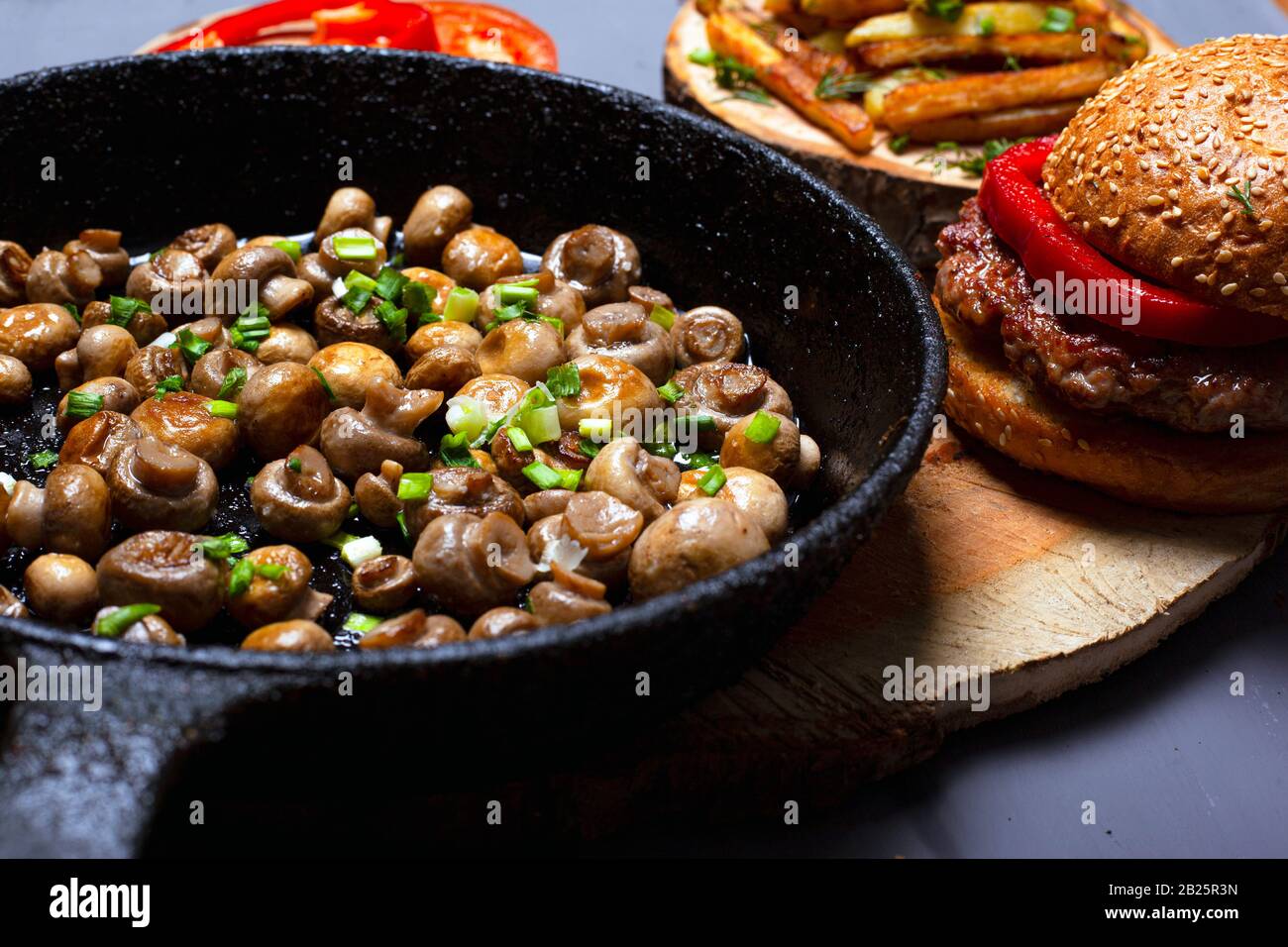 Champignons frits d'or : Champignon dans une poêle noire et un hamburger juteux, délicieux appétissant maison, nourriture grasse sur fond gris. Banque D'Images
