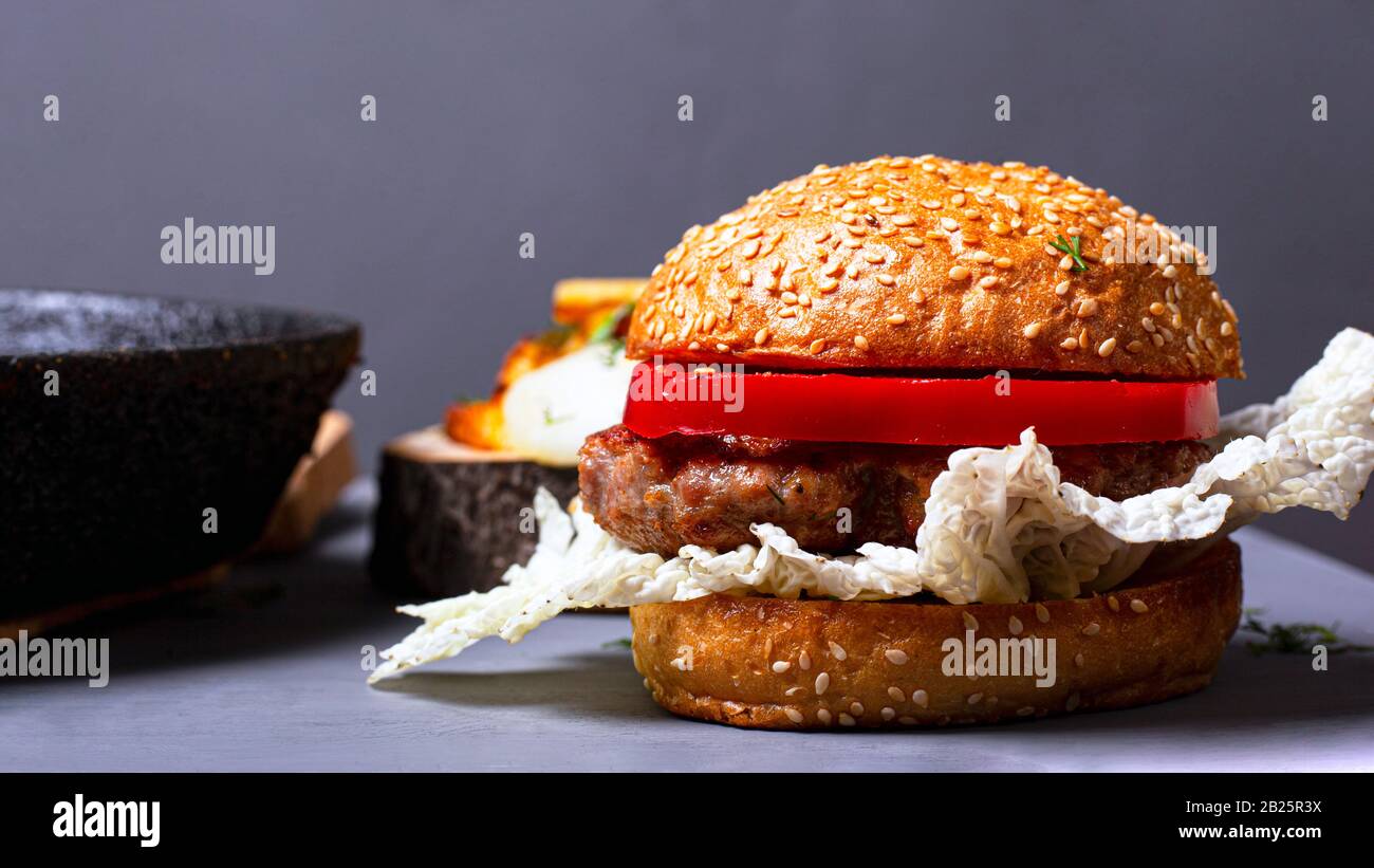 hamburger classique maison avec chou chinois, côtelette juteuse et poivre sucré sur fond gris. Banque D'Images