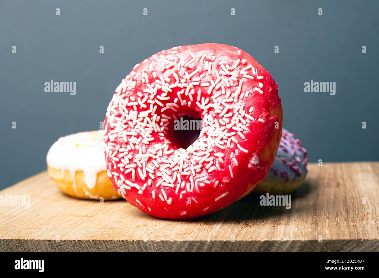 délicieusement savoureux beignet rouge avec poudre blanche sur un support en bois sur fond gris. gros plan. Banque D'Images