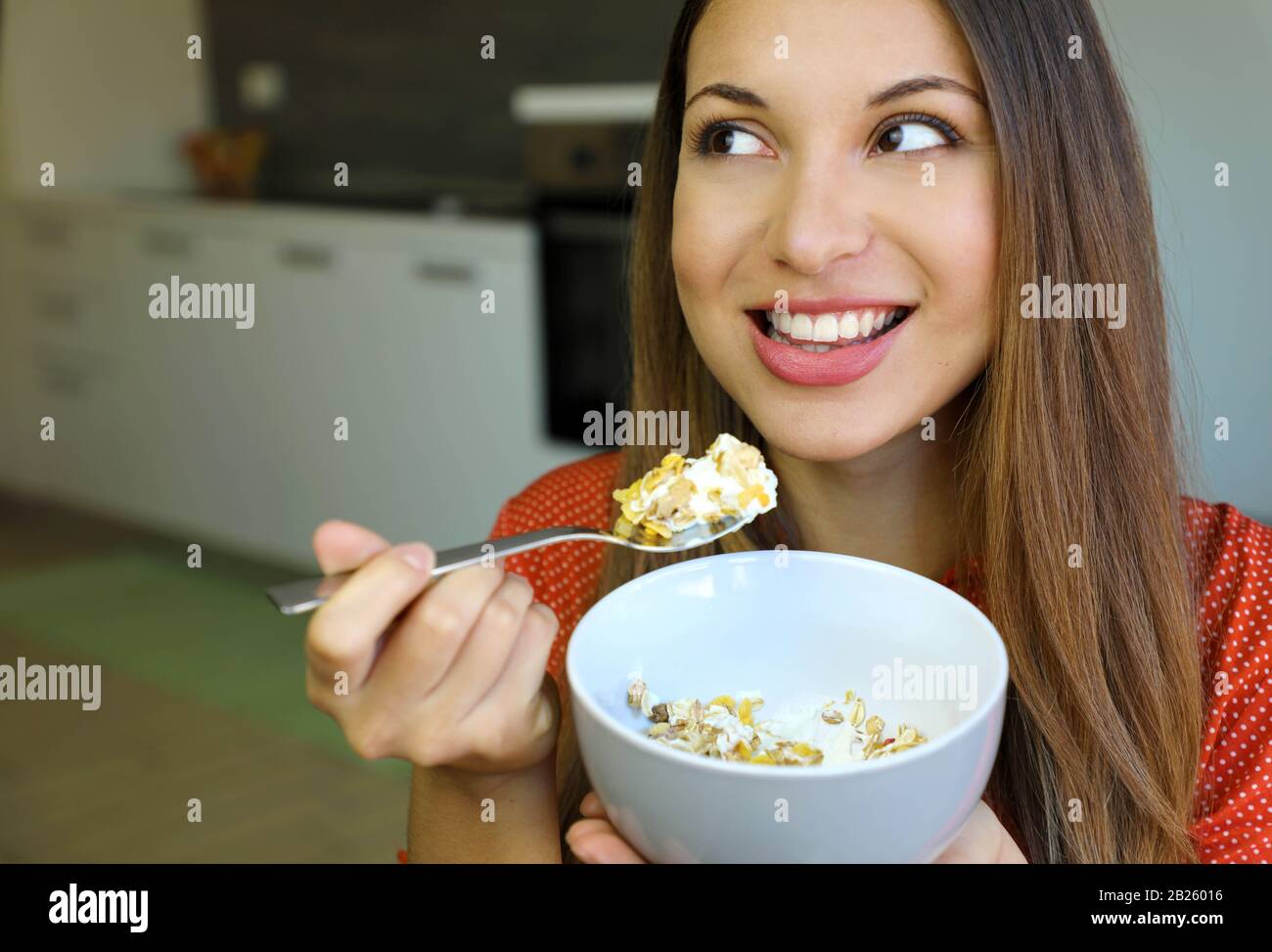 Gros plan sur la belle jeune femme mangeant des yaourts skyr avec des céréales muesli fruits à la maison, regardant sur le côté, se concentrer sur les yeux modèles, image intérieure. H Banque D'Images