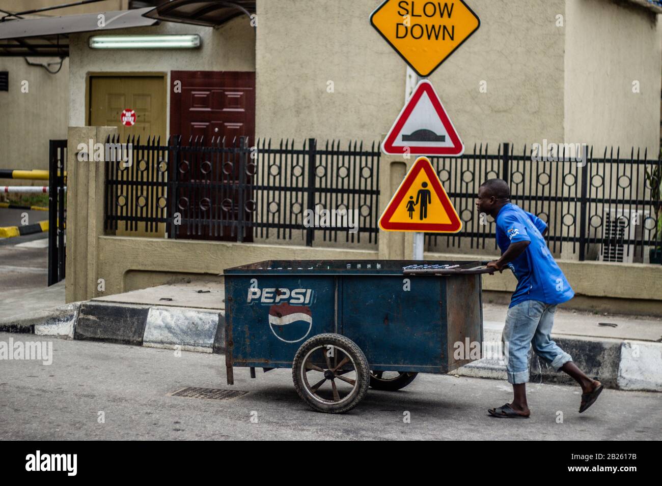 Un homme poussant une roue rectangulaire barrow avec le logo Pepsi dans une rue à Lagos, au Nigeria. Banque D'Images