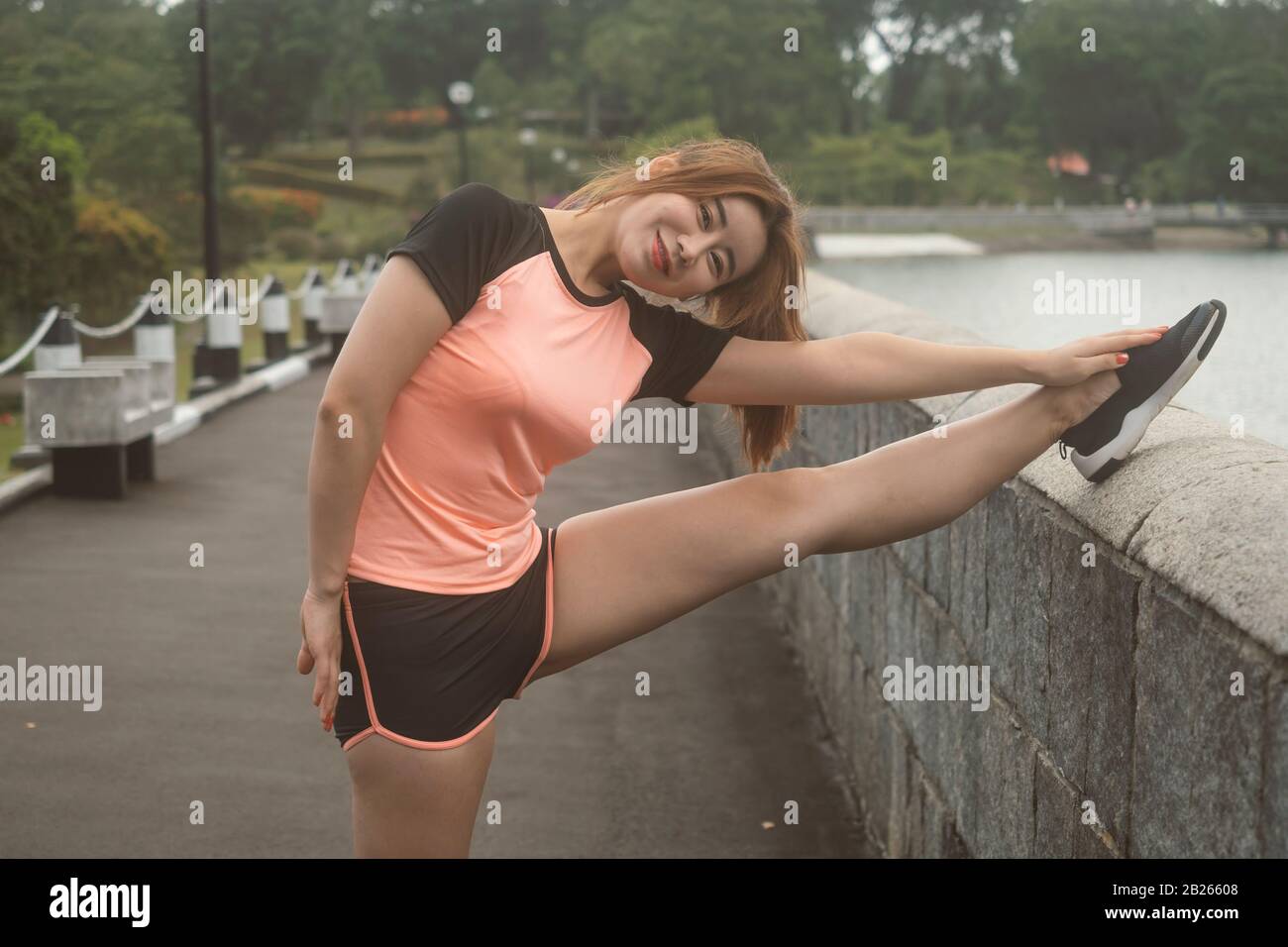 Une fille chinoise asiatique qui fait des jambes s'étire dans sa tenue de sport avant de courir dans le parc naturel tôt le matin Banque D'Images