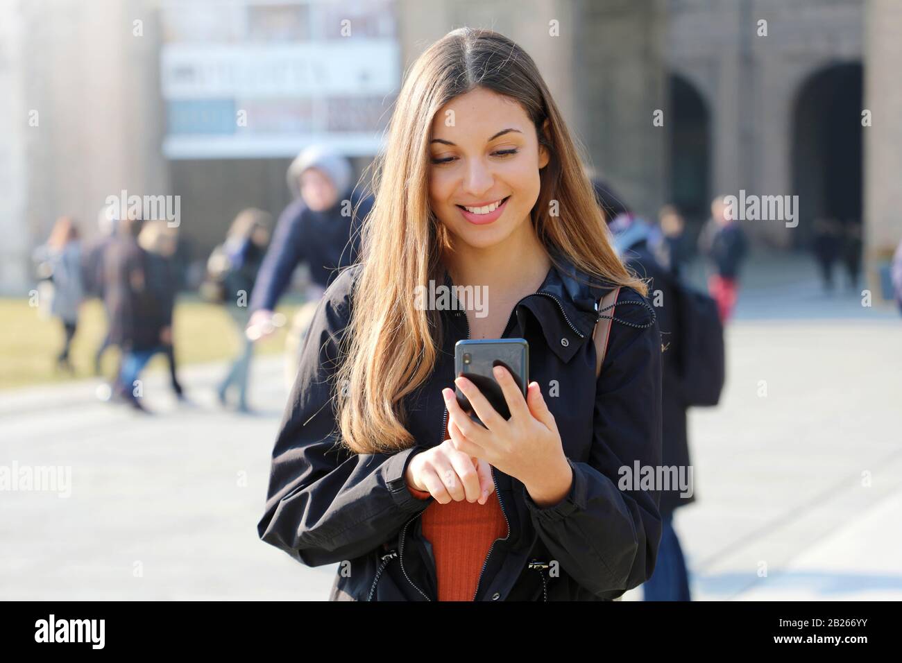 Bonne jeune fille du lycée avec smartphone à l'extérieur le jour ensoleillé du printemps texting et sourire Banque D'Images