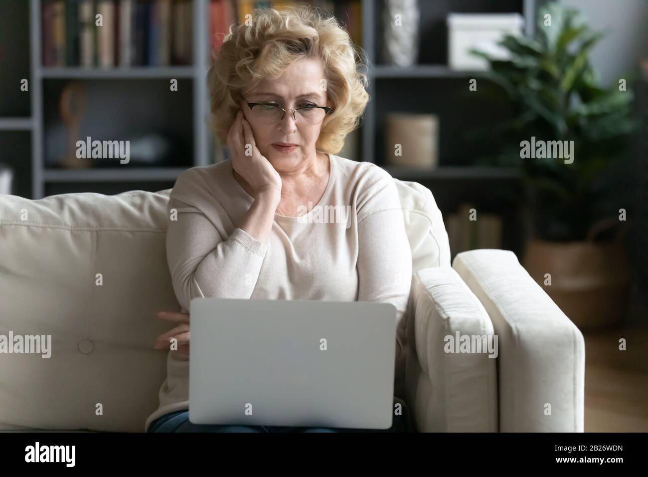 Une femme âgée inquiète a lu de mauvaises nouvelles sur un ordinateur portable Banque D'Images