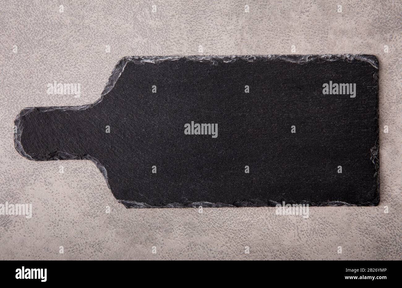 Vue plate sur la couche naturelle de roche noire rugueuse servant de planche sur une surface grise texturée pour l'arrière-plan. Banque D'Images