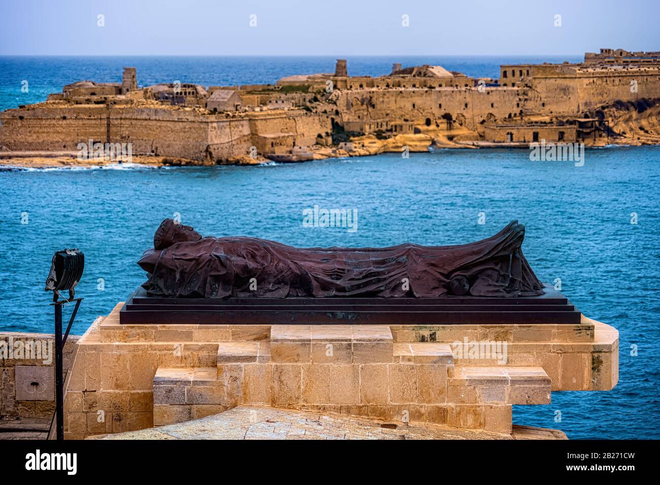 Sculpture à couchette au mémorial de la guerre de Siege Bell à la Valette, Malte, fort Ricasoli à Kalkara en arrière-plan Banque D'Images