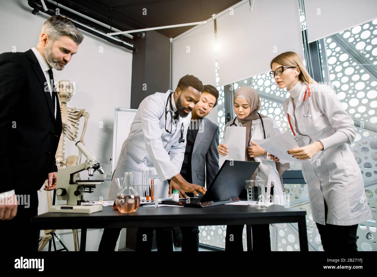 Équipe multiethnique de médecins, scientifiques, travailleurs de la santé ayant une discussion, tout en utilisant un ordinateur portable, parler des résultats de l'essai clinique ou Banque D'Images