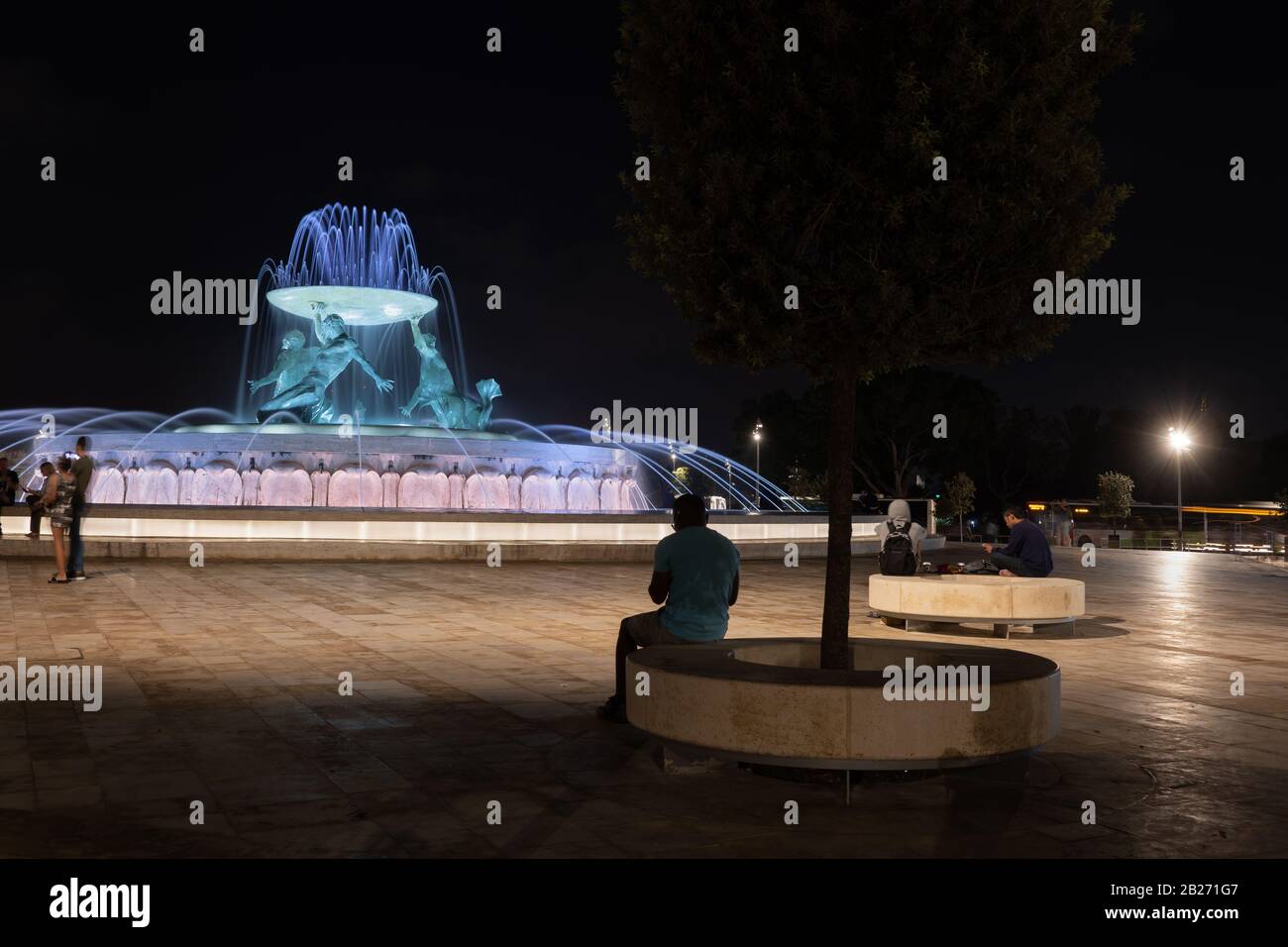 Les gens apprécient une soirée tranquille à la fontaine des Tritons illuminée la nuit sur une place près de la ville de la Valette à Malte Banque D'Images