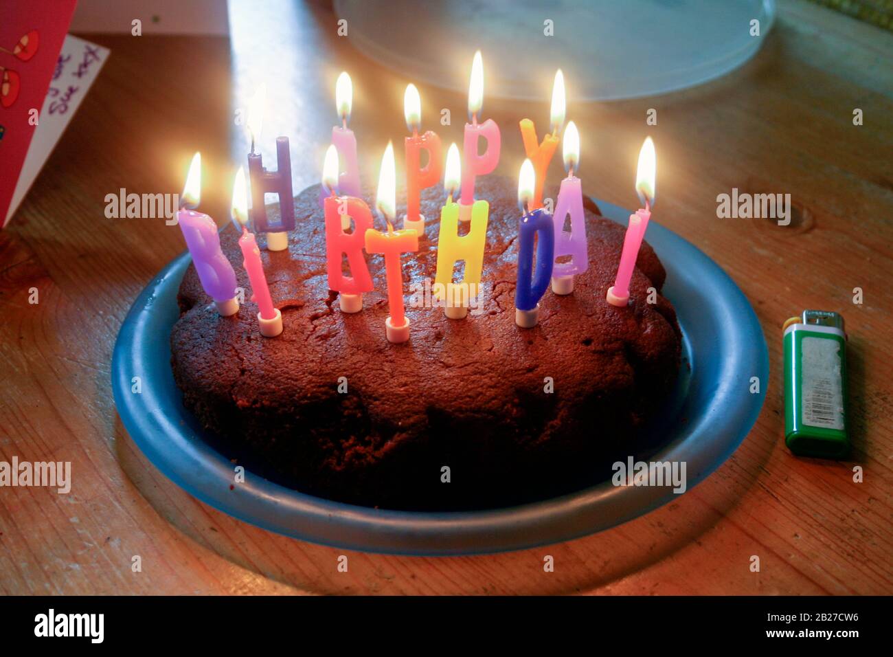 Un gâteau fait maison sur une plaque en plastique avec des bougies illuminées orthographiant les mots « Happy Birthday » à la fête d'un enfant Banque D'Images