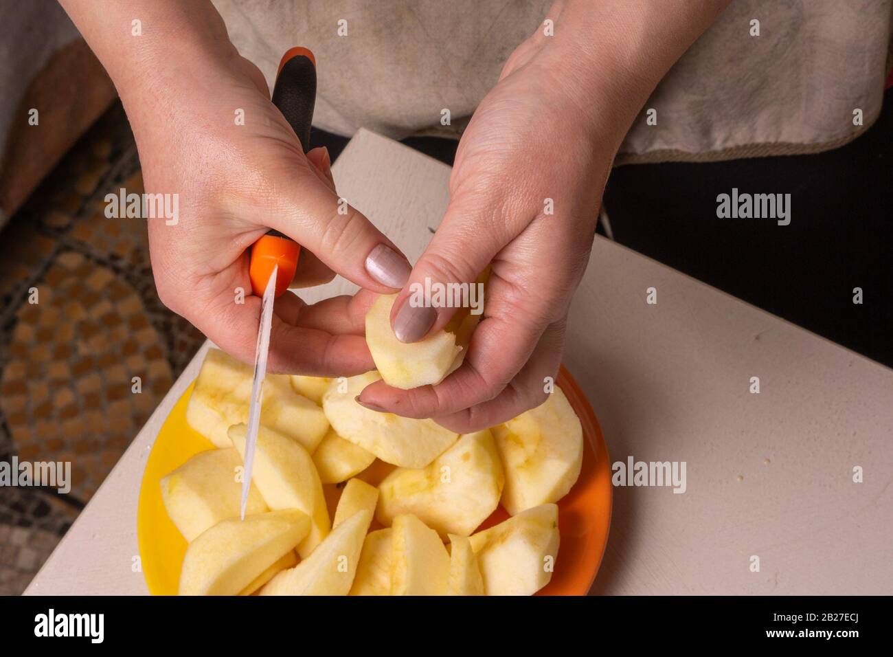 Mains d'une femme âgée pelant une pomme avec un couteau en céramique blanc. Banque D'Images