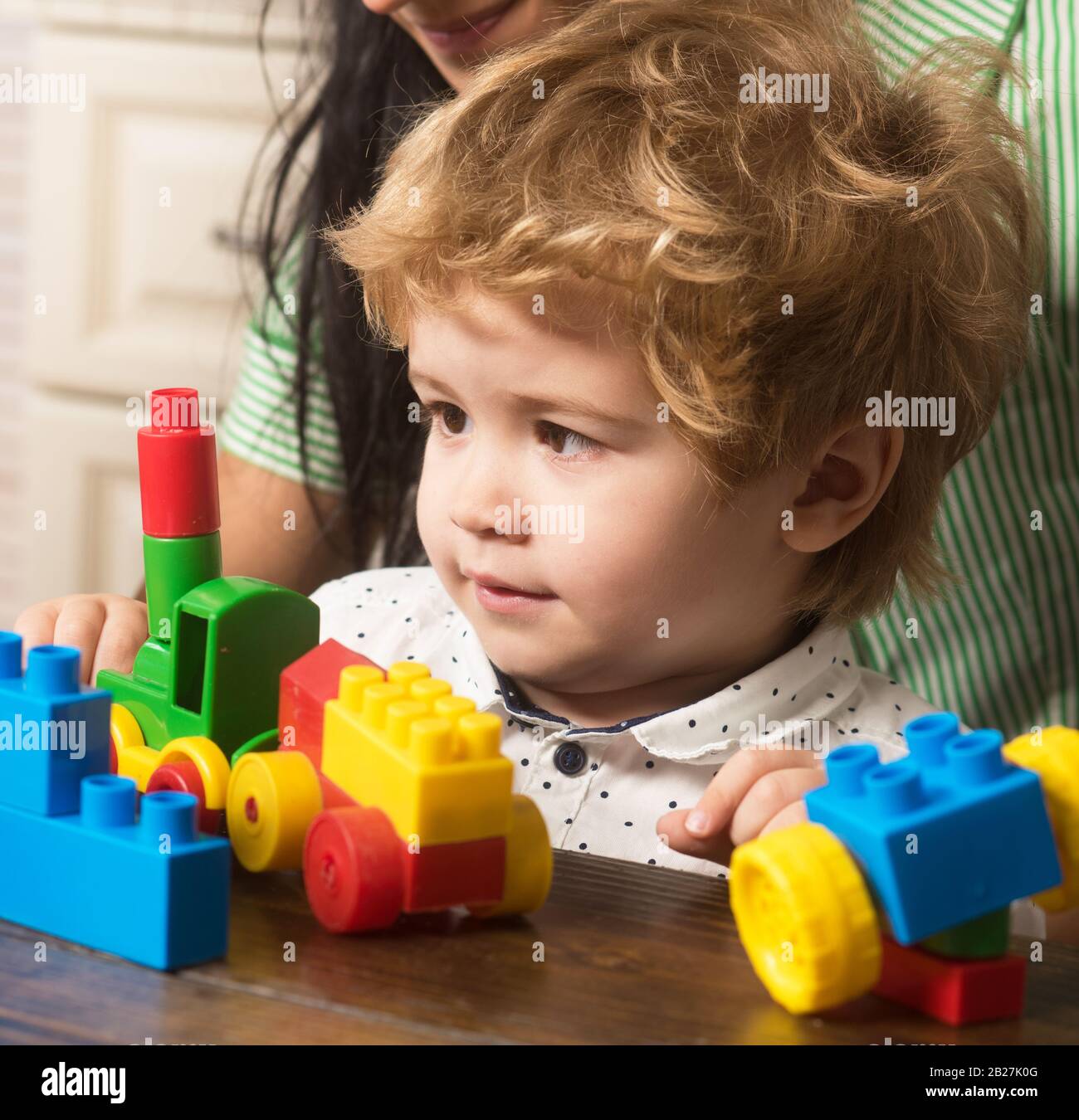 Bébé garçon regarde le train jouet fait de blocs de construction. Les  enfants jouent avec des briques en plastique colorées sur la table. Enfant  près de maman sur fond en bois clair,