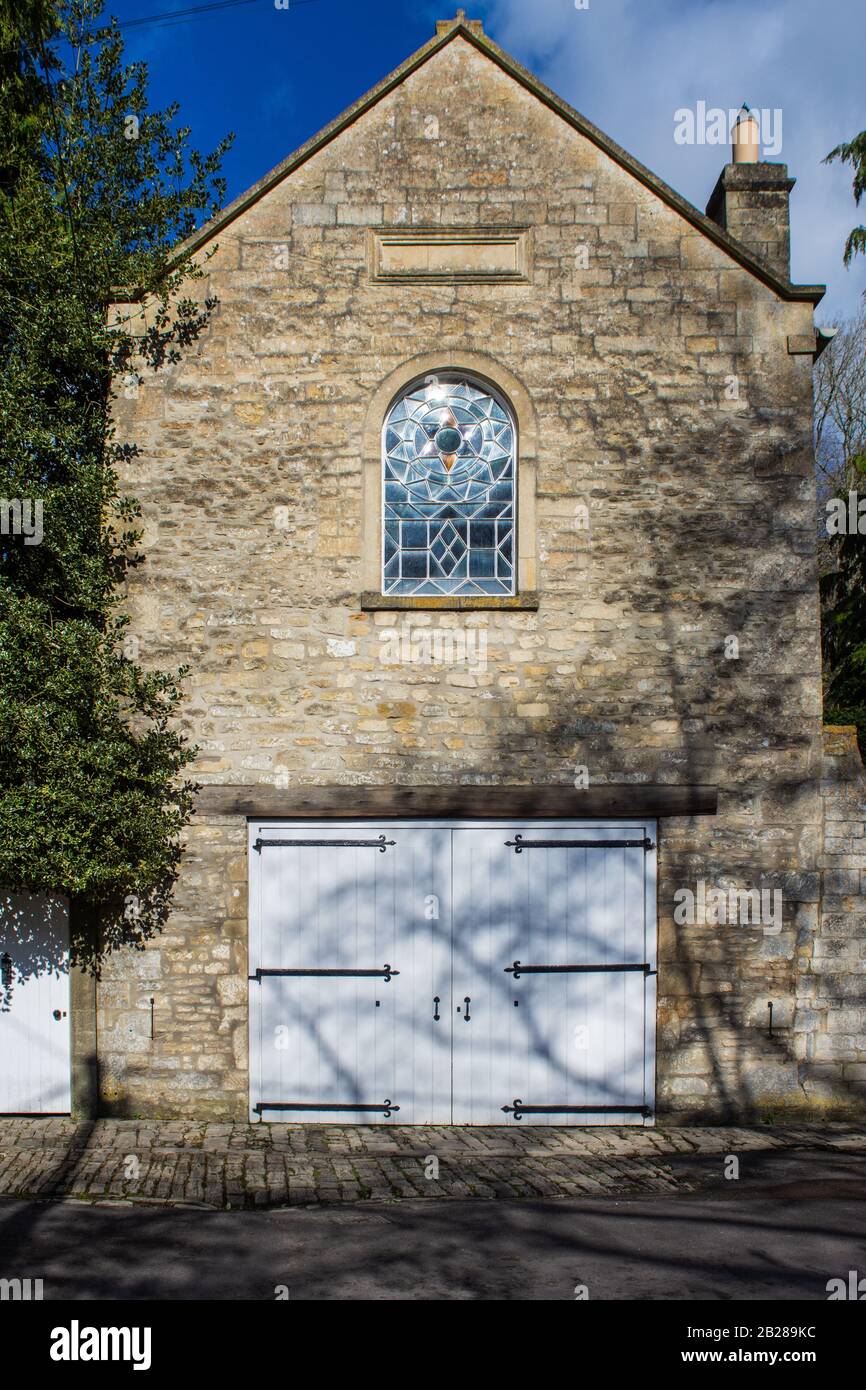 Une maison d'autocar reconvertie avec une fenêtre vitrail au-dessus des portes de transport avec de longues charnières en fer dans le style plus plat-de-lis dans le hameau de Turleigh in Banque D'Images