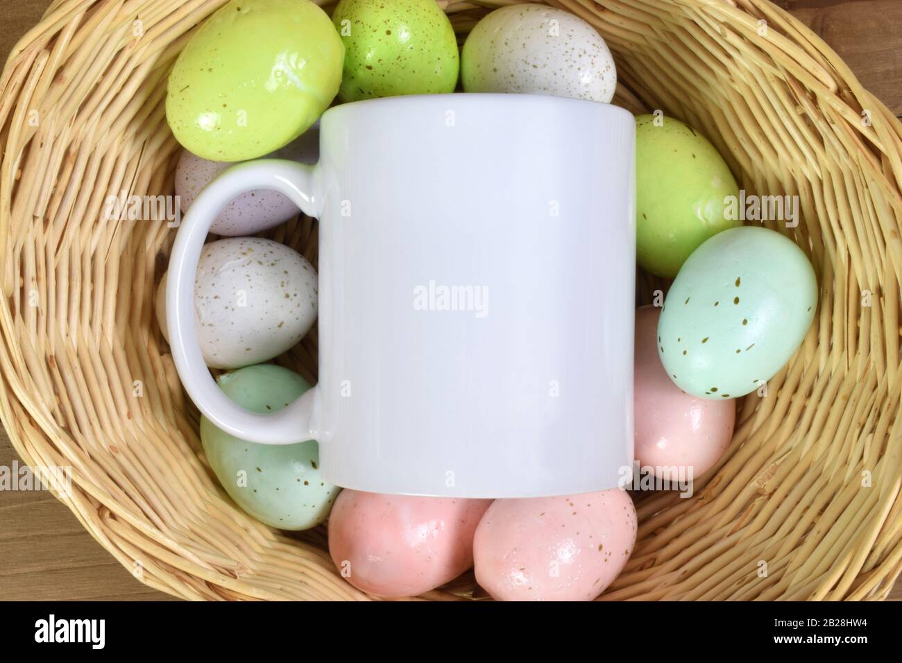 Une tasse de 11 onces avec une tasse de café blanc vierge au sommet d'œufs de Pâques mouchetés colorés à l'intérieur d'un panier tissé. Banque D'Images