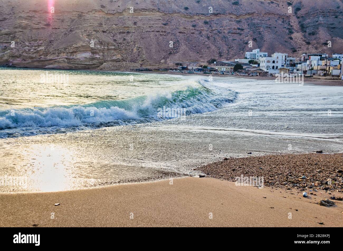 Vagues sur la plage près d'une petite ville sur la vallée des montagnes, le matin. De Muscat, Oman. Banque D'Images